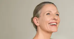 Sofwave in Mt Pleasant, SC in the sentence A smiling mature woman with her hair in a bun looking upward, showcasing healthy skin.